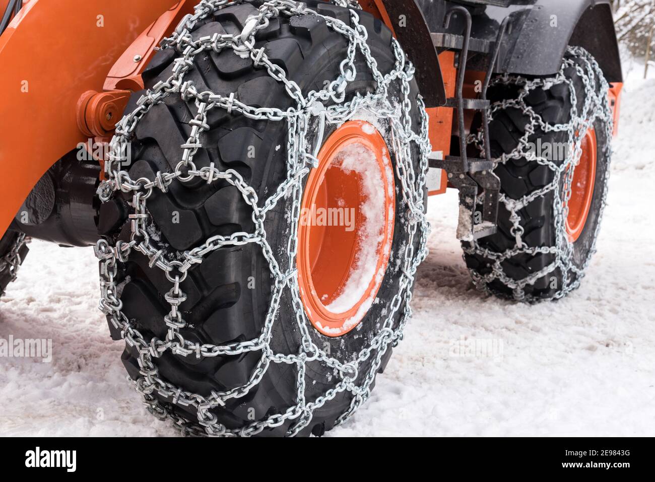 Metal snow chains wrapped around wheel tires of bulldozer car parked on snowy road Stock Photo