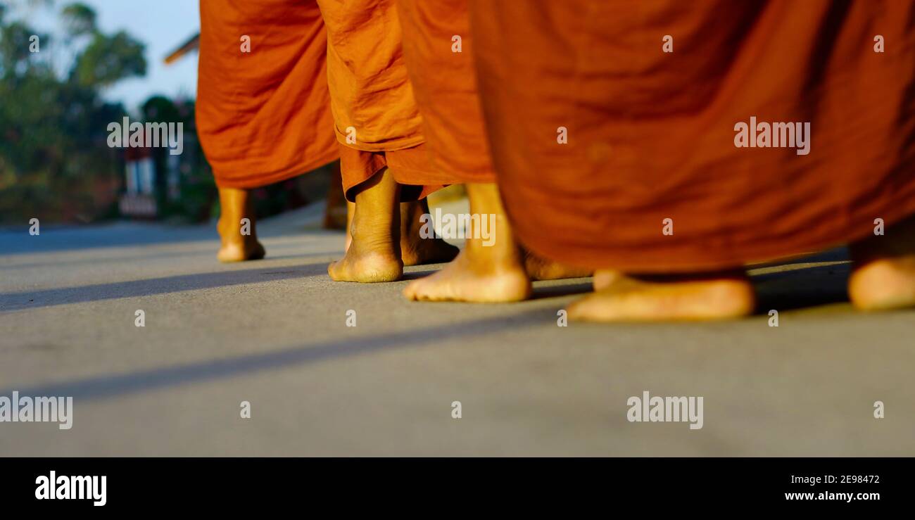 feet of monks dressing orange robe during reception of alms, around buddhist temple Stock Photo