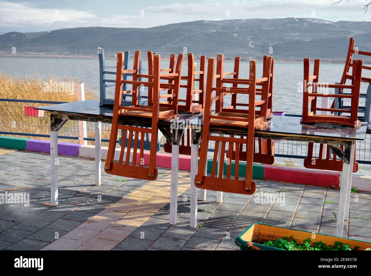Cute cafe near the lake and sea is closed due to the pandemic with lake and mountain background. Old and wooden chairs staying on table.Colorful photo Stock Photo