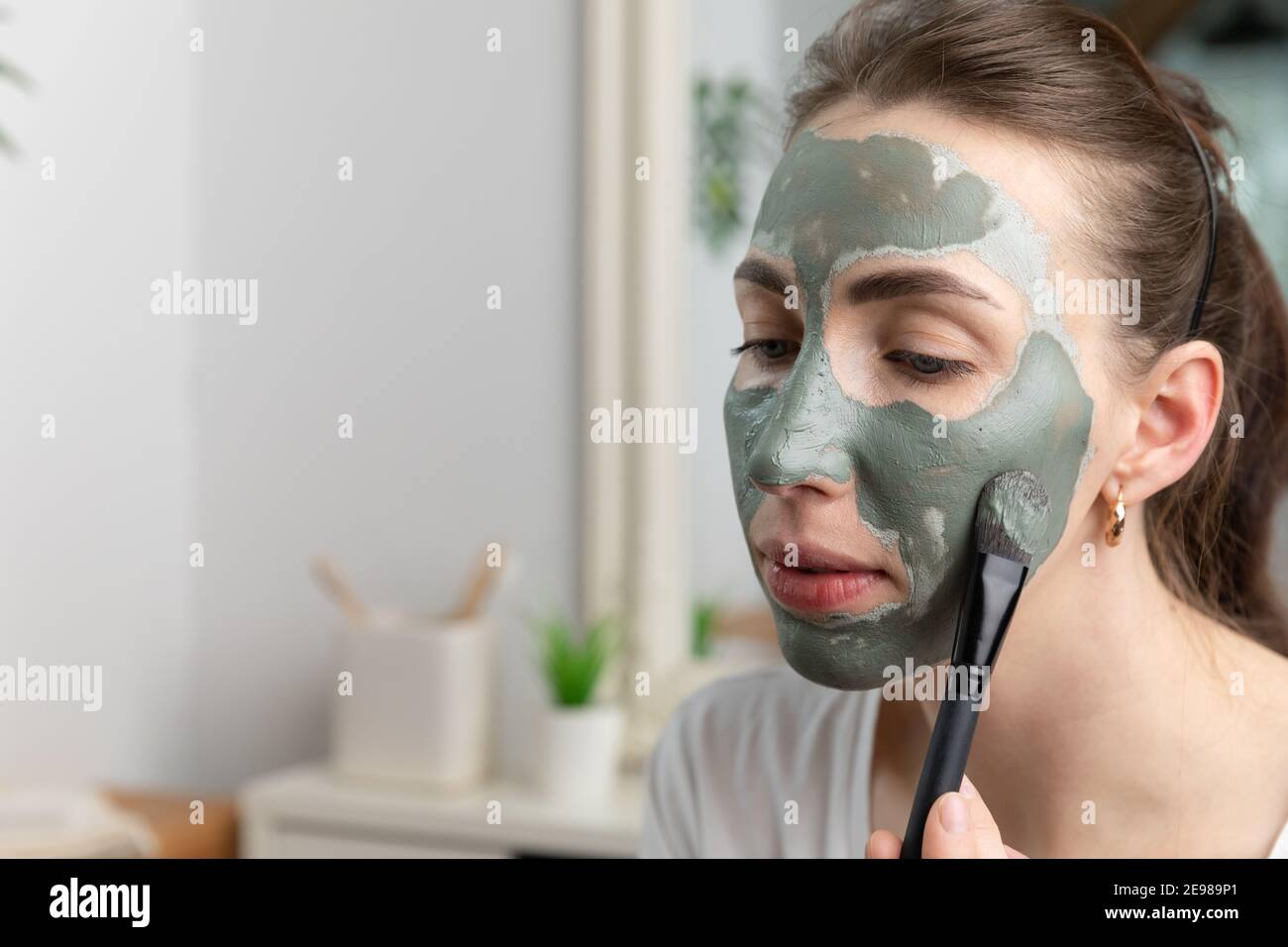 Close up of a beautiful women applying green clay facial mask. Brush touching her skin. Beauty and skin care concept. Stock Photo