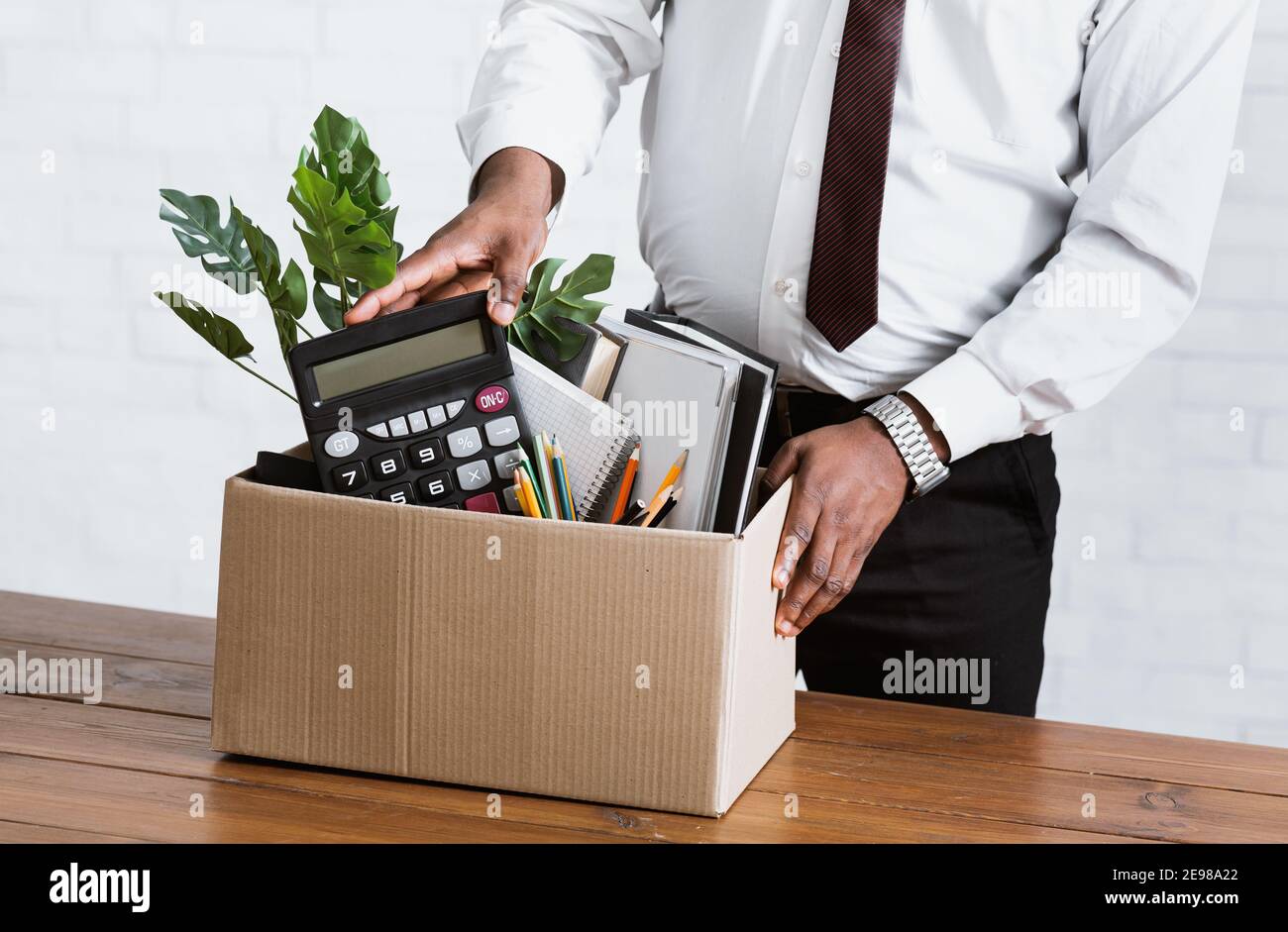 Unrecognizable black guy collecting his office stuff into carton box. Economic crisis and unemployment Stock Photo