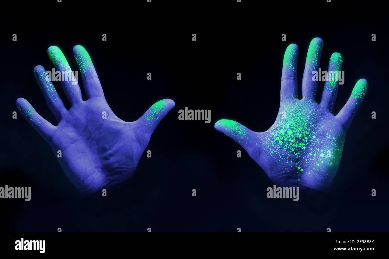 Human hands glowing from UV ultra violet light showing bacteria and viruses on a black background, showing the importance of hand washing. Stock Photo