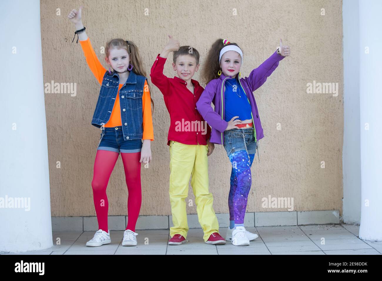 Children pose for a photo shoot. Boy and two little girls models in bright clothes are looking at the camera. Stock Photo