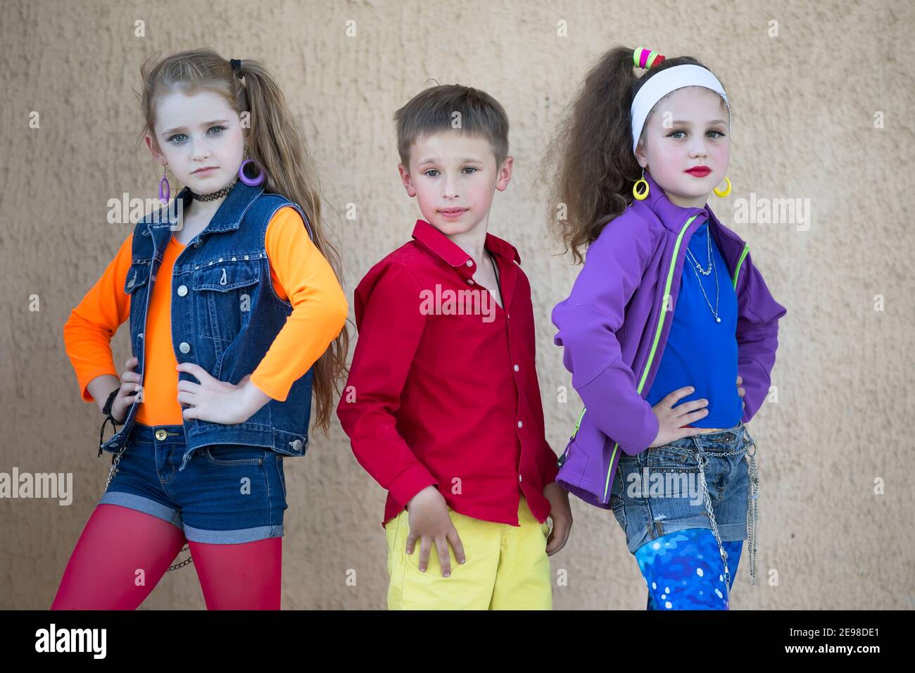 Children pose for a photo shoot. Boy and two little girls models in bright clothes are looking at the camera. Stock Photo