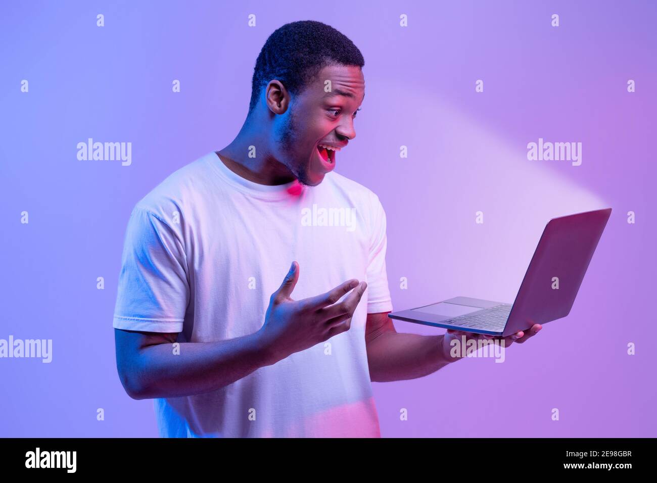 Online Offer. Surprised African Man Holding Laptop Looking At Glowing Screen Stock Photo