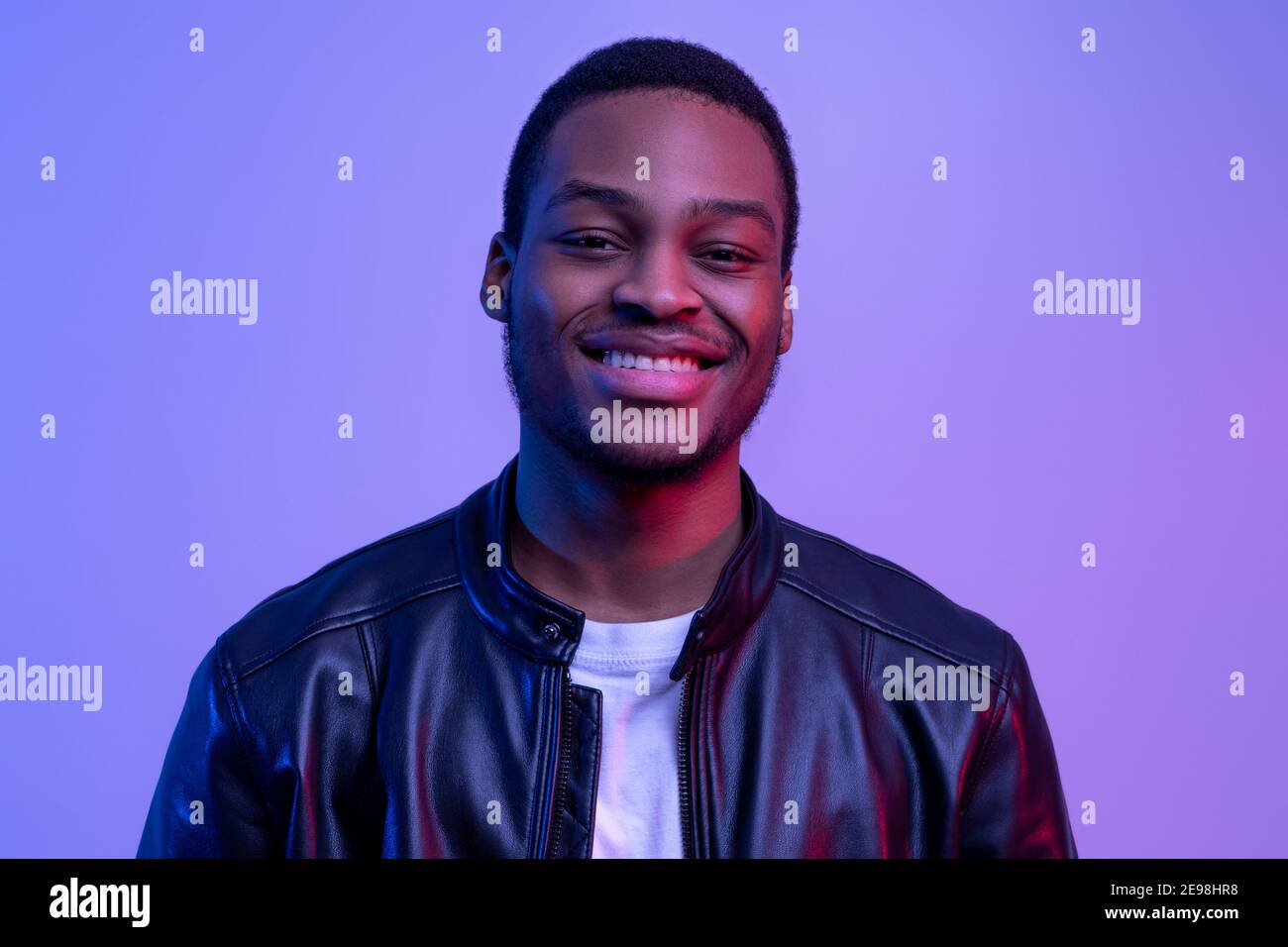 Portraif Of Happy Black Guy Posing In Leather Jacket Under Neon Light Stock Photo