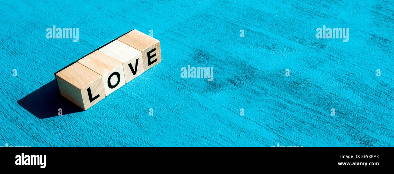 Valentin's day and happy emotion concept: On left, the word LOVE written with single wooden cube letters made for board games on blue textured surface Stock Photo
