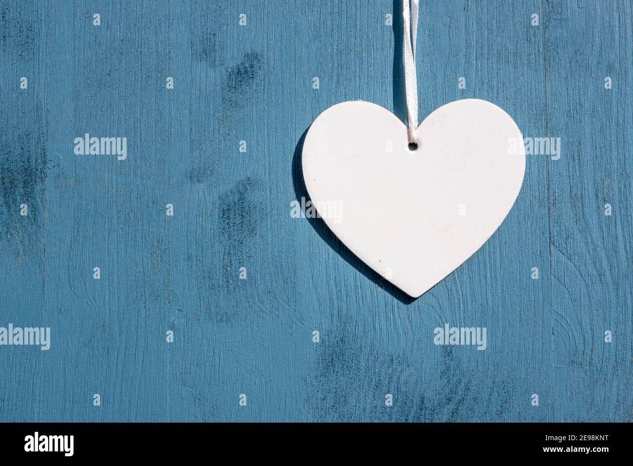 Love and greetings concept: Top view on a single white empty heart hanging over a wooden blue background with copy space. Celebration for friends Stock Photo