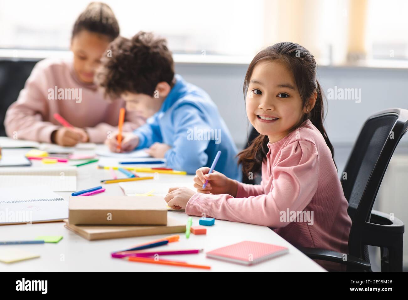 Smiling asian school girl sitting at desk in classroom Stock Photo