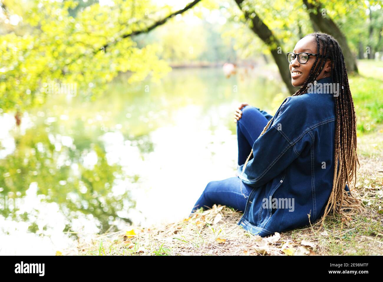 Outdoor portrait of beautiful happy laughing mixed race African American girl teenager female young woman sitting in the park near river Stock Photo