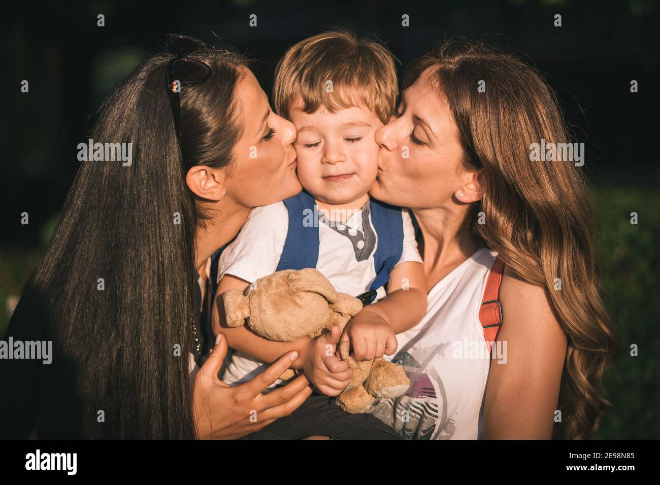 Mom and aunt holding and kissing cute, little boy. Family love Stock Photo