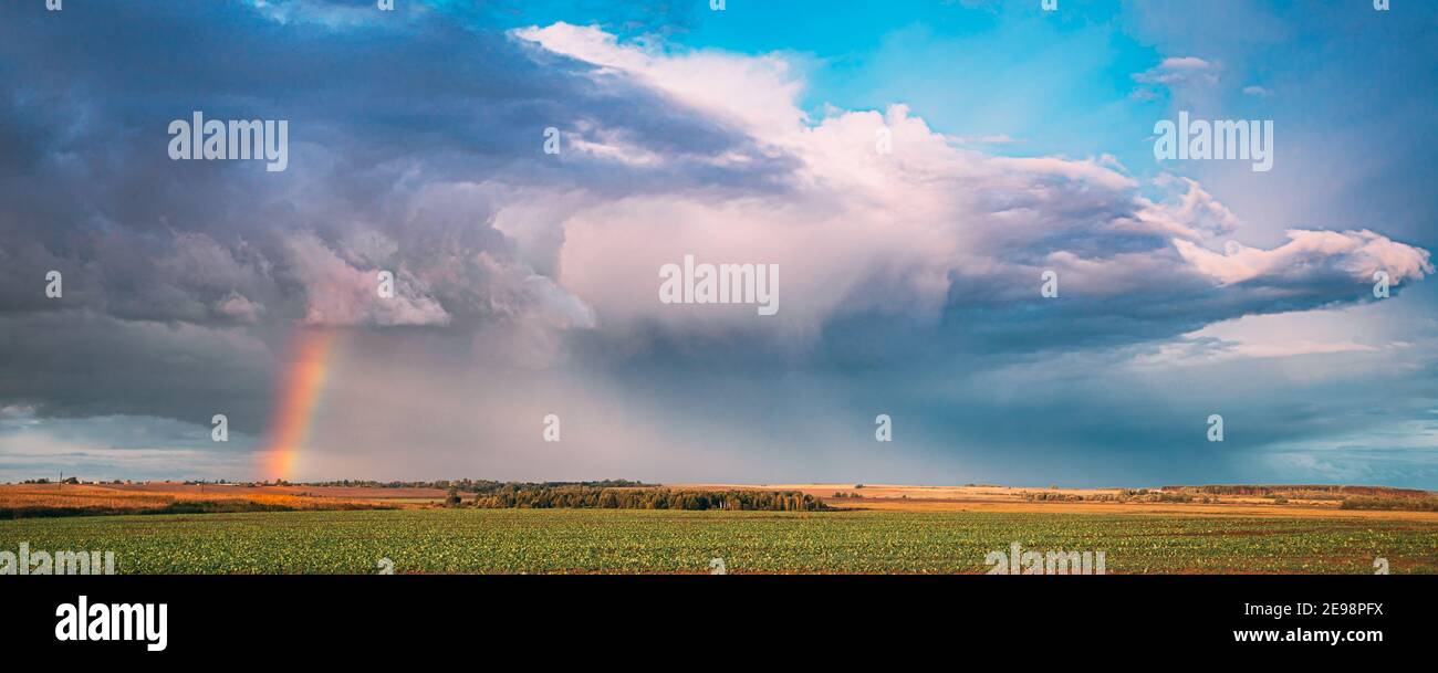 Dramatic Sky During Rain With Rainbow On Horizon Above Rural Landscape