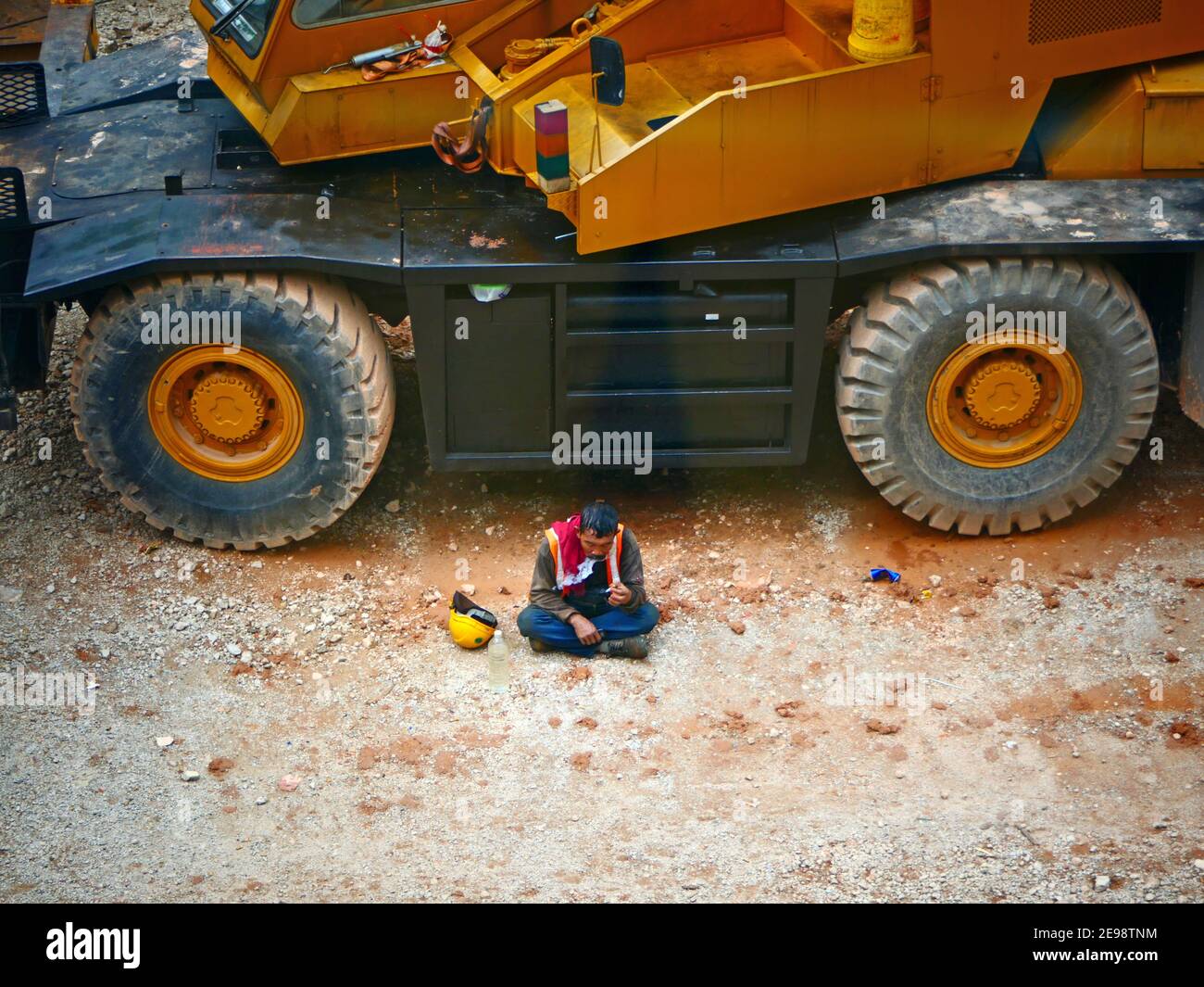 Construction worker resting smoking under a bog truck, Kuala Lumpur Malaysia Stock Photo