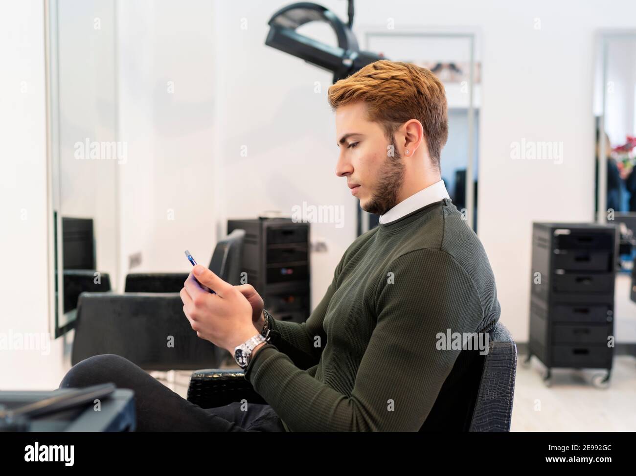 young man using his smartphone at the hairdresser Stock Photo