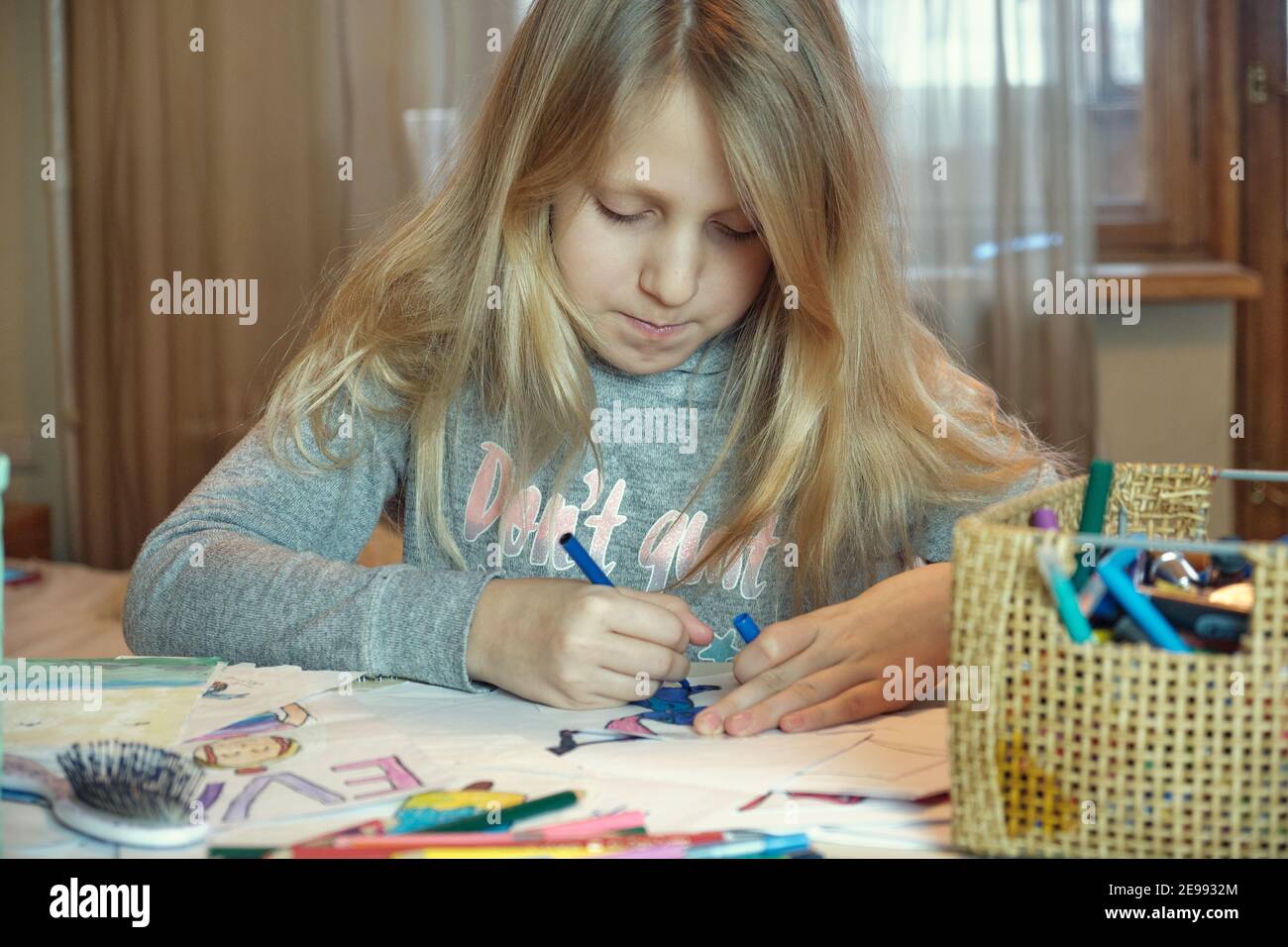 Little blonde girl drawing on her book and having fun at playtable. Child girl does her school homework at home. Stock Photo