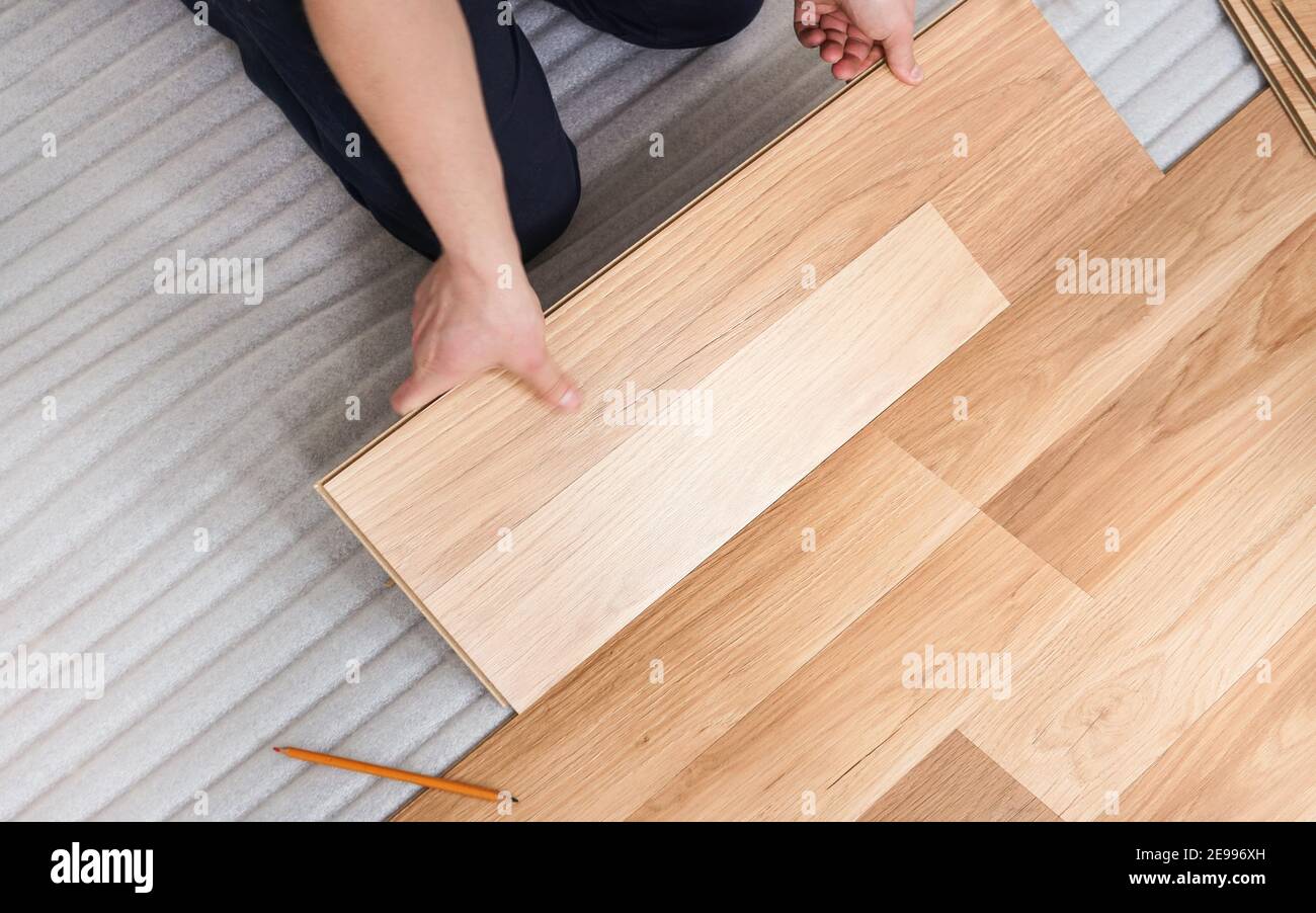 Installing laminated floor, detail view from above on man hands holding wooden tile, fitting it, over white foam base layer Stock Photo