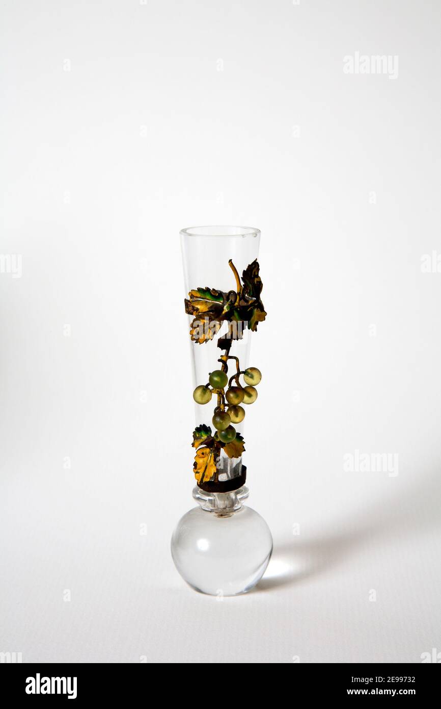 A small piece of antique glassware with strapped decoration of a vine with round solid glass base possibly used as a single flower vase. Stock Photo