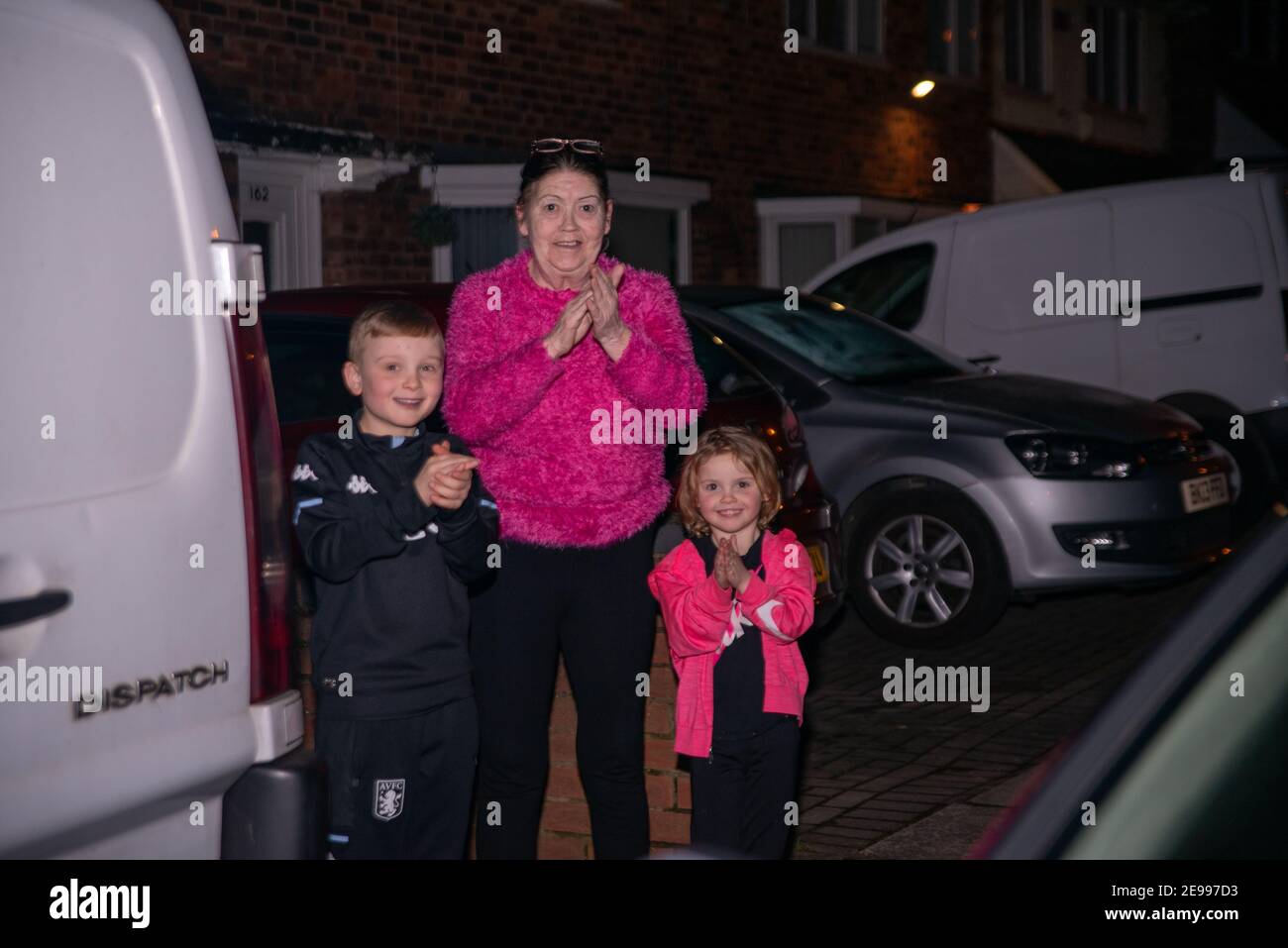 Birmingham, West Midlands, UK. 3rd February 2021: A lady and two young children stand clapping at the end of their driveway at 6PM, after Boris Johnson called for the nation to pay respects to Captain Tom Moore who passed away at the age of 100 on Tuesday, after a fight with Covid-19. (Parental consent provided for children in photograph) Credit: Ryan Underwood / Alamy Live News Stock Photo