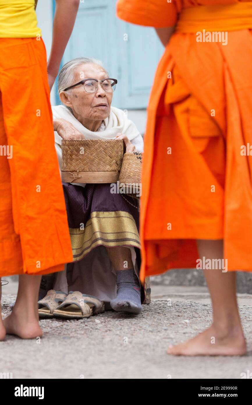 Luang Prabang, Laos Old woman handing out rice in Tak Bat or The monk's morning alms procession. Stock Photo