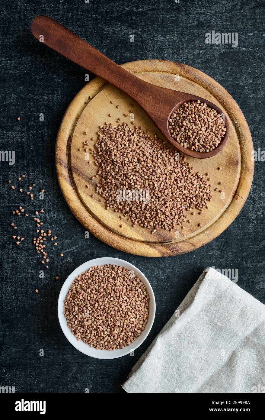 Buckwheat on cutting board, in wooden spoon and ceramic bowl, gluten free ancient grain for healthy eating, flat lay Stock Photo