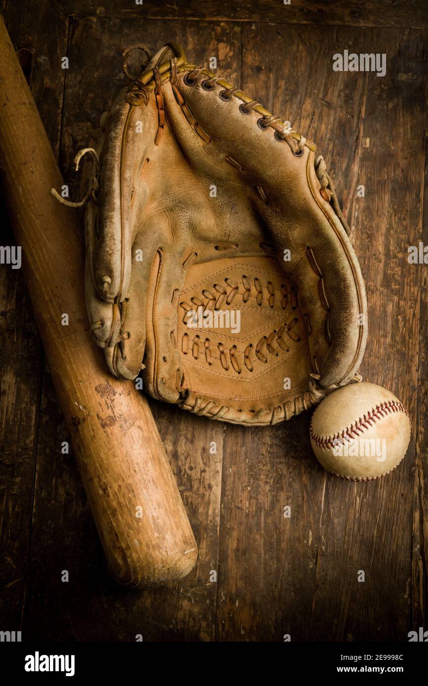 Old leather baseball glove lying on an antique table with ball and bat