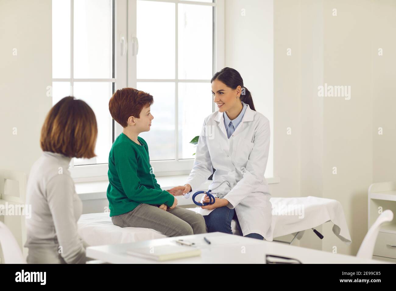Female pediatrician talks to a little boy who came for a medical examination with his mother. Stock Photo