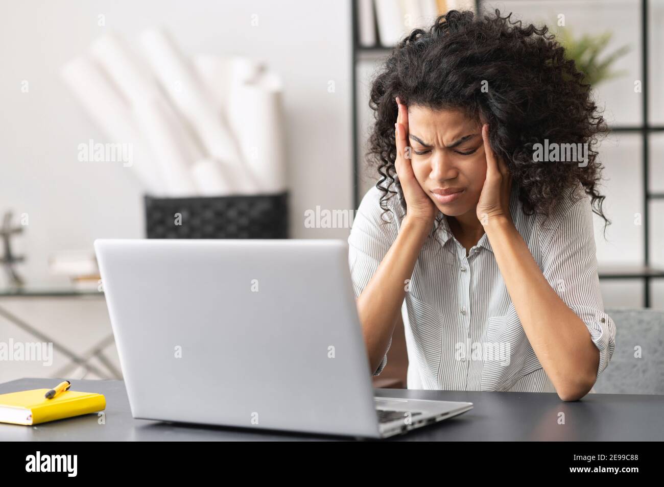 Exhausted millennial African American female office worker touching temples, does not understand the task, suffering from severe headache or migraine Stock Photo