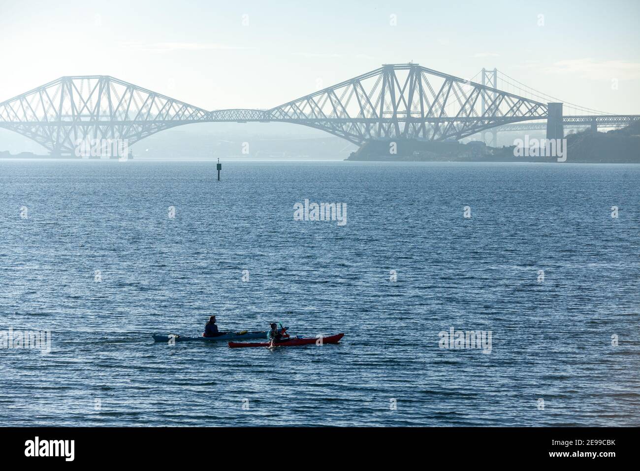 Two sea kayakers paddling just off the coast at Dalgety Bay near the Forth Bridge, Fife, Scotland Stock Photo