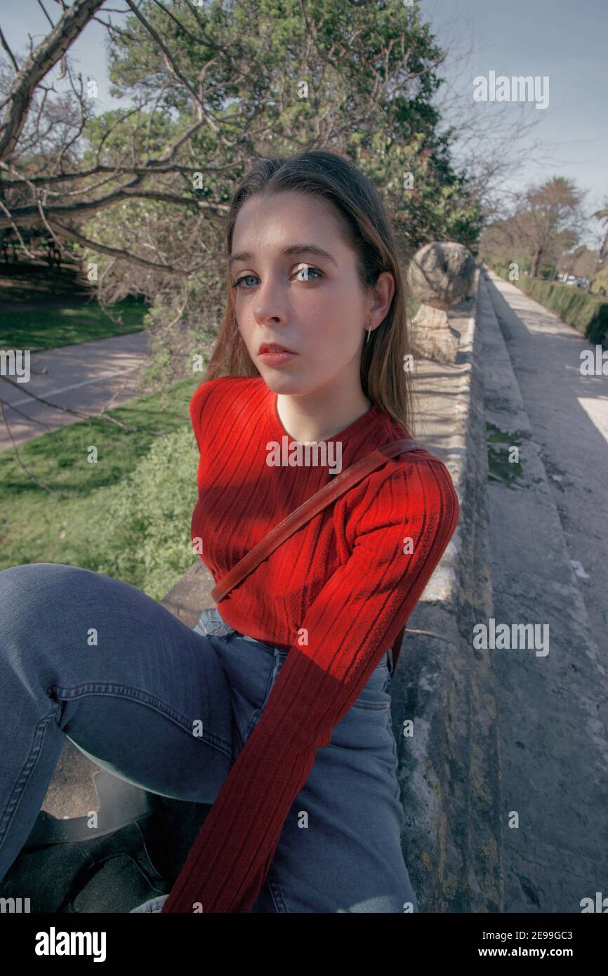Angular picture of young thoughtful woman looking in front at the camera in a winter sunny day while sitting on a bench in side of a park.Seasonal Stock Photo