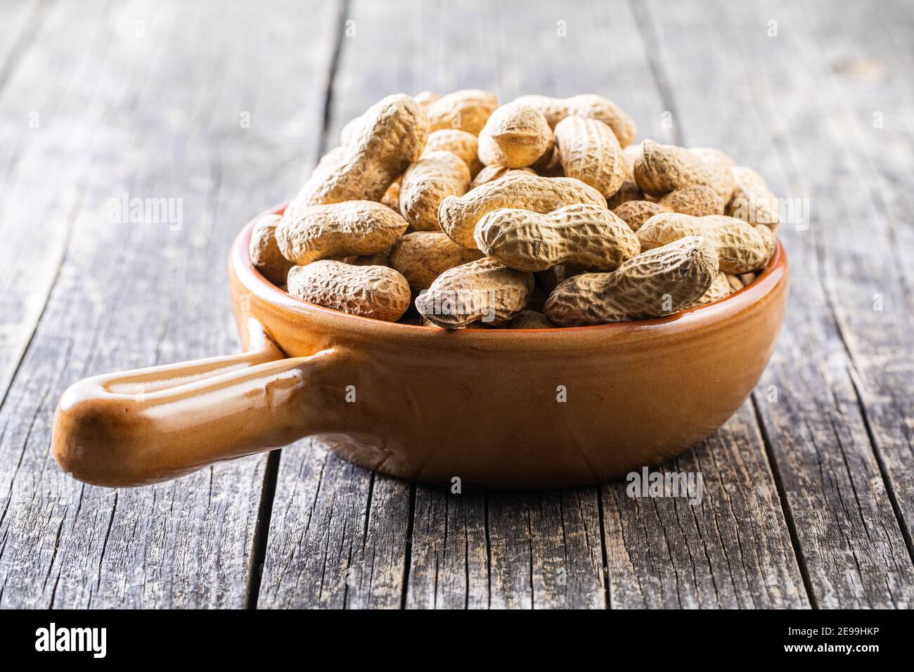 Roasted peanuts. Tasty groundnuts in pot on wooden table. Stock Photo