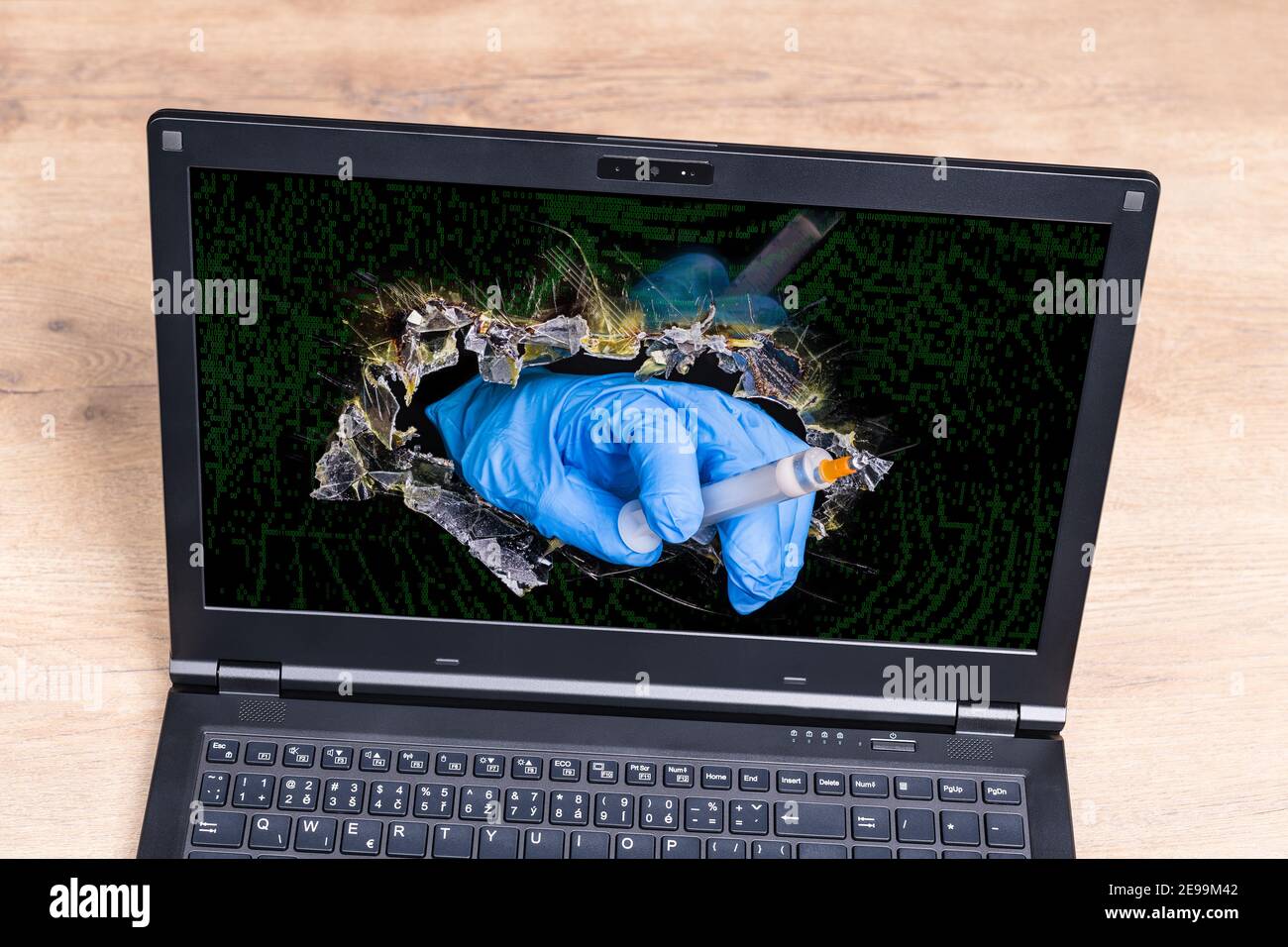 Syringe with covid-19 vaccine in doctor hand sticking out of broken laptop desktop. Virtual healthcare professional inside a hole in digital monitor. Stock Photo