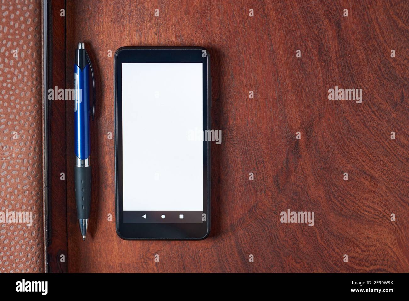 Black mobile phone with blank white screen, pen and notebook on rustic wooden table. Minimalistic top view of office setup, workspace with space for t Stock Photo
