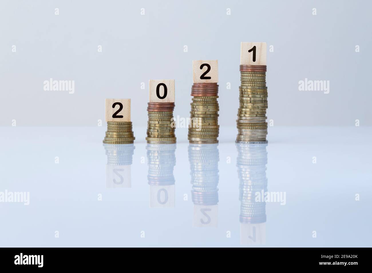 Number 2021 on wooden blocks on top of ascending stacks of coins on gray background. Concept of increase of wealth, economy, financial growth&success. Stock Photo