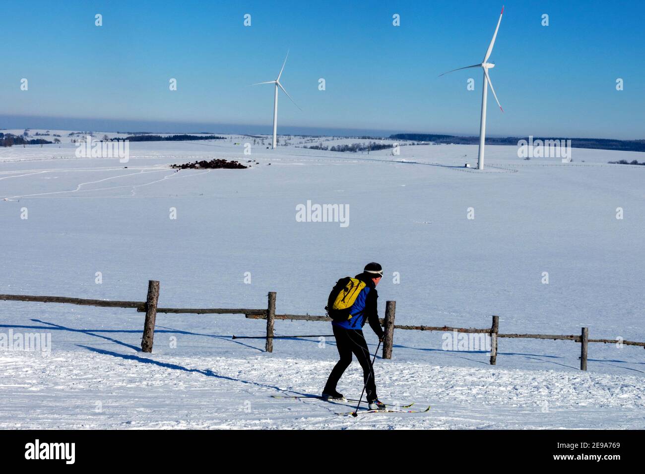 Skier cross country skiing in a snowy landscape, two wind turbines in the background, Czech-German border Stock Photo