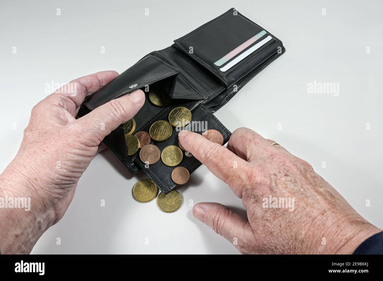 Elderly hands counting the few euro coins in a wallet, money concept for old age poverty and financial crisis, light gray background, selected focus, Stock Photo