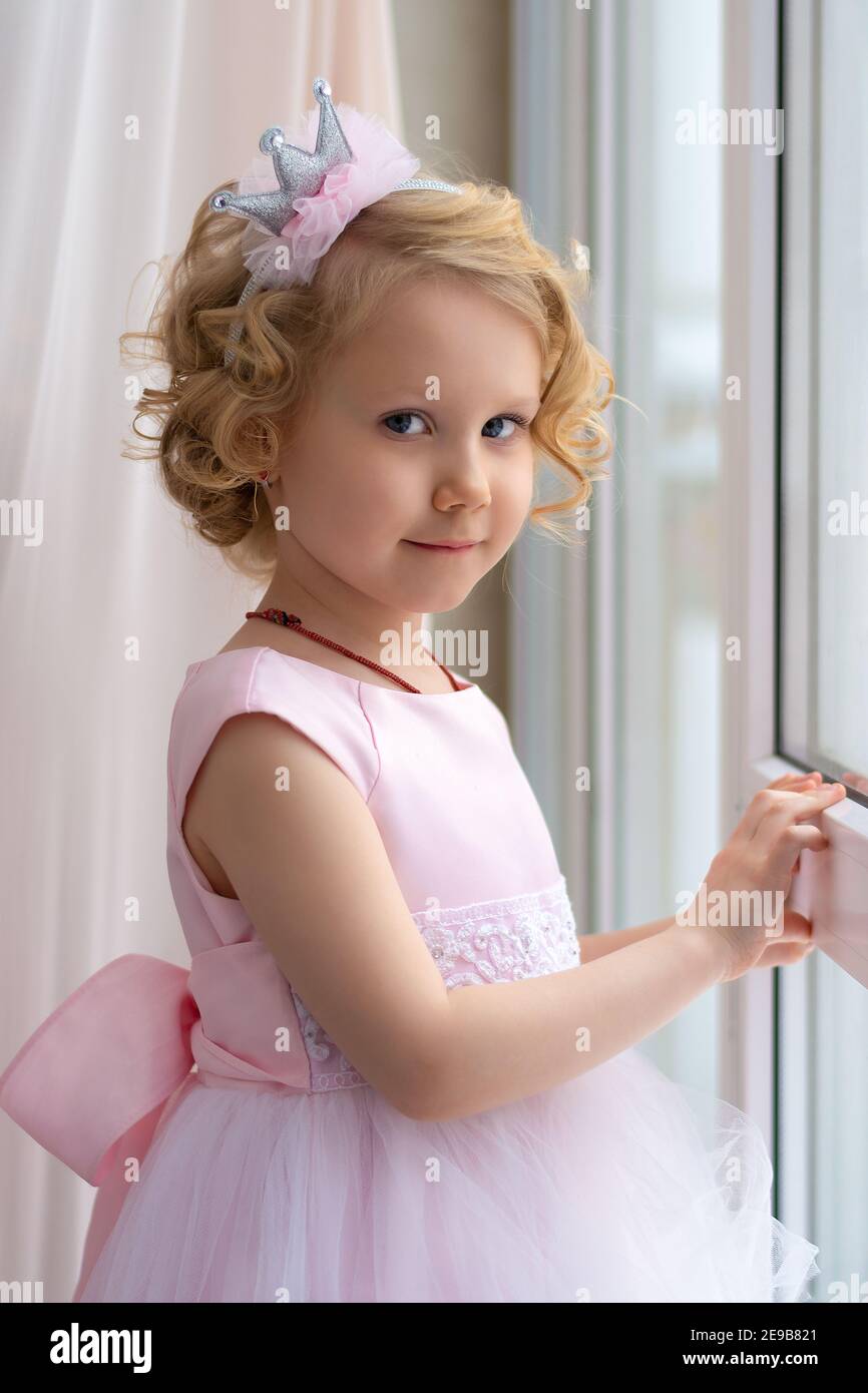 a little girl in a pink dress and a crown smiles near the window Stock ...