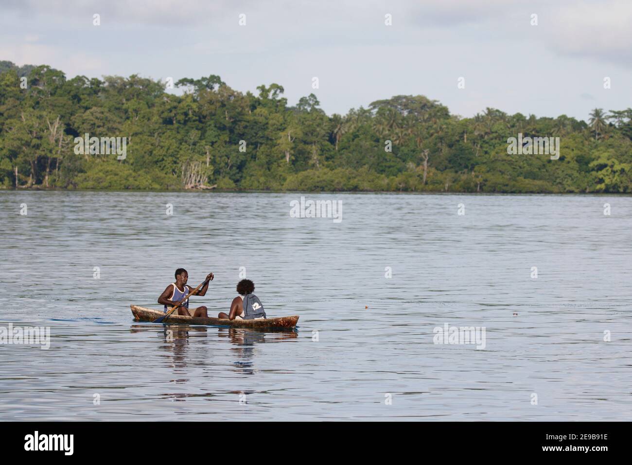 Horizontal view of dugout canoe with two people aboard and vegetated