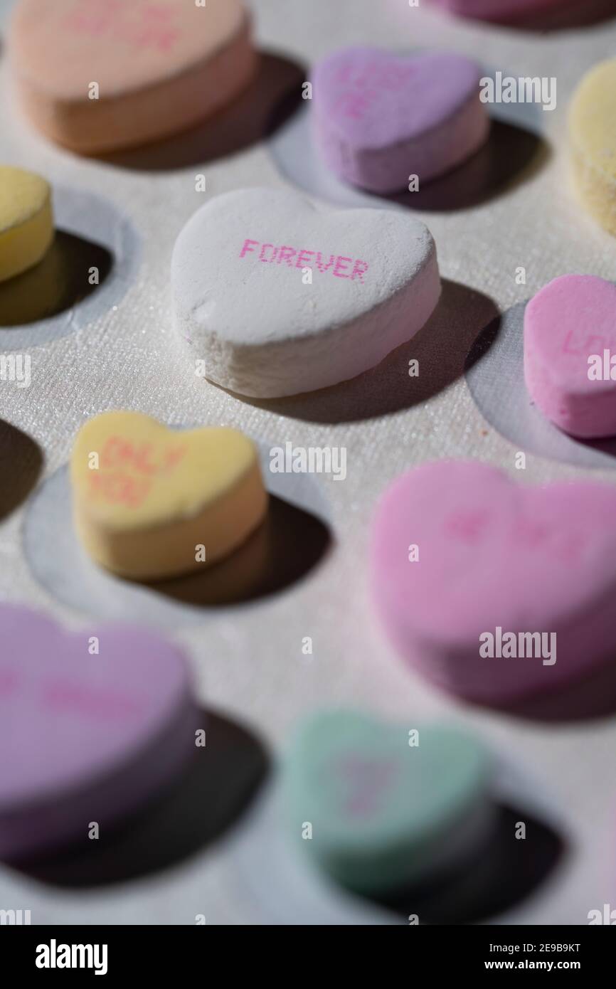 Rows of colorful conversation candy hearts lined up in rows on a white surface with one heart in focus reading 'Forever' Stock Photo