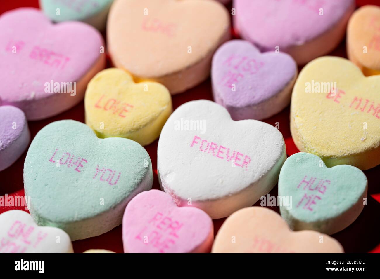 Rows of colorful conversation candy hearts lined up in rows on a red surface. Stock Photo
