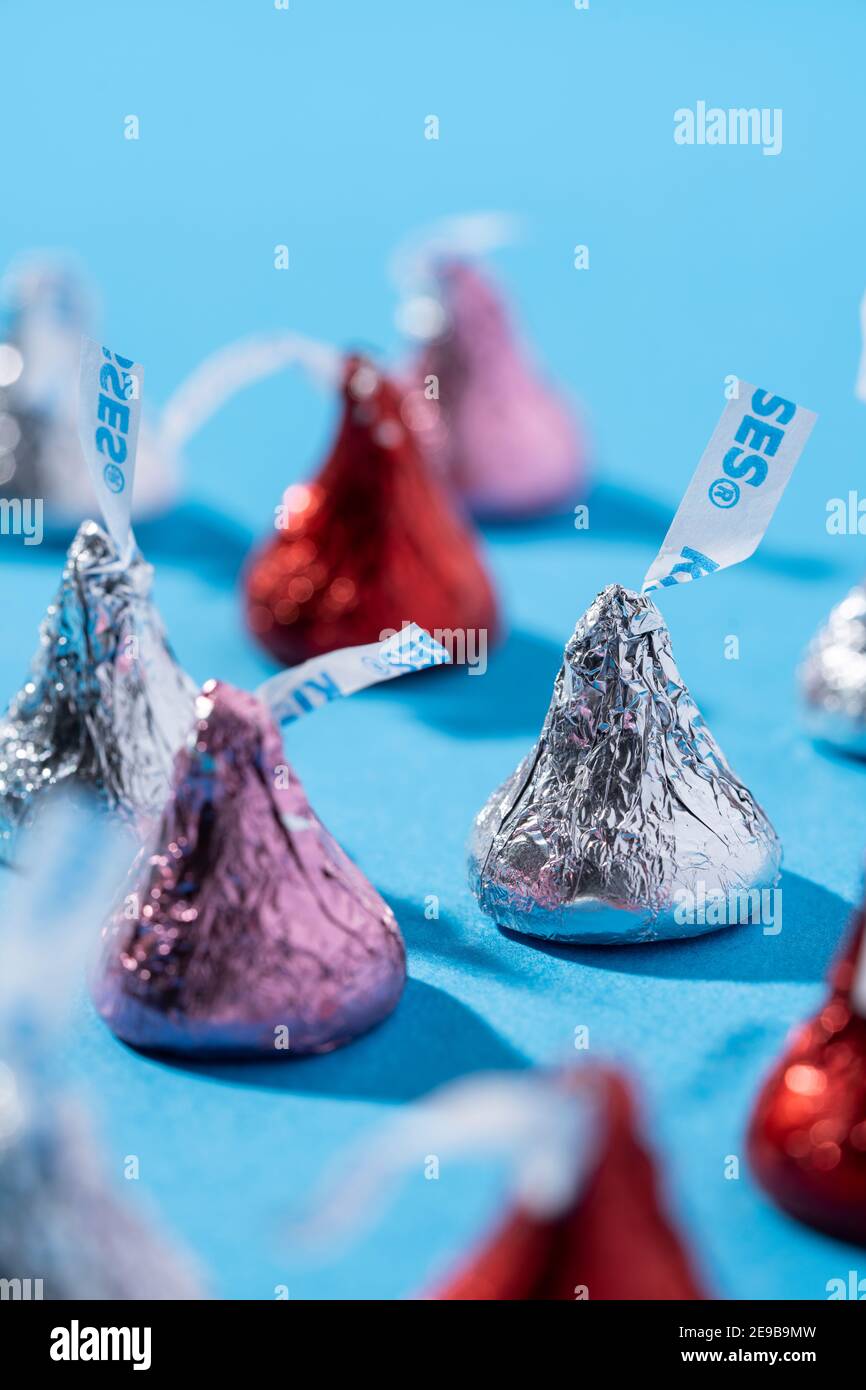 A bunch of Hershey Kisses in red, pink, and silver wrappers, sit on a  blue surface Stock Photo