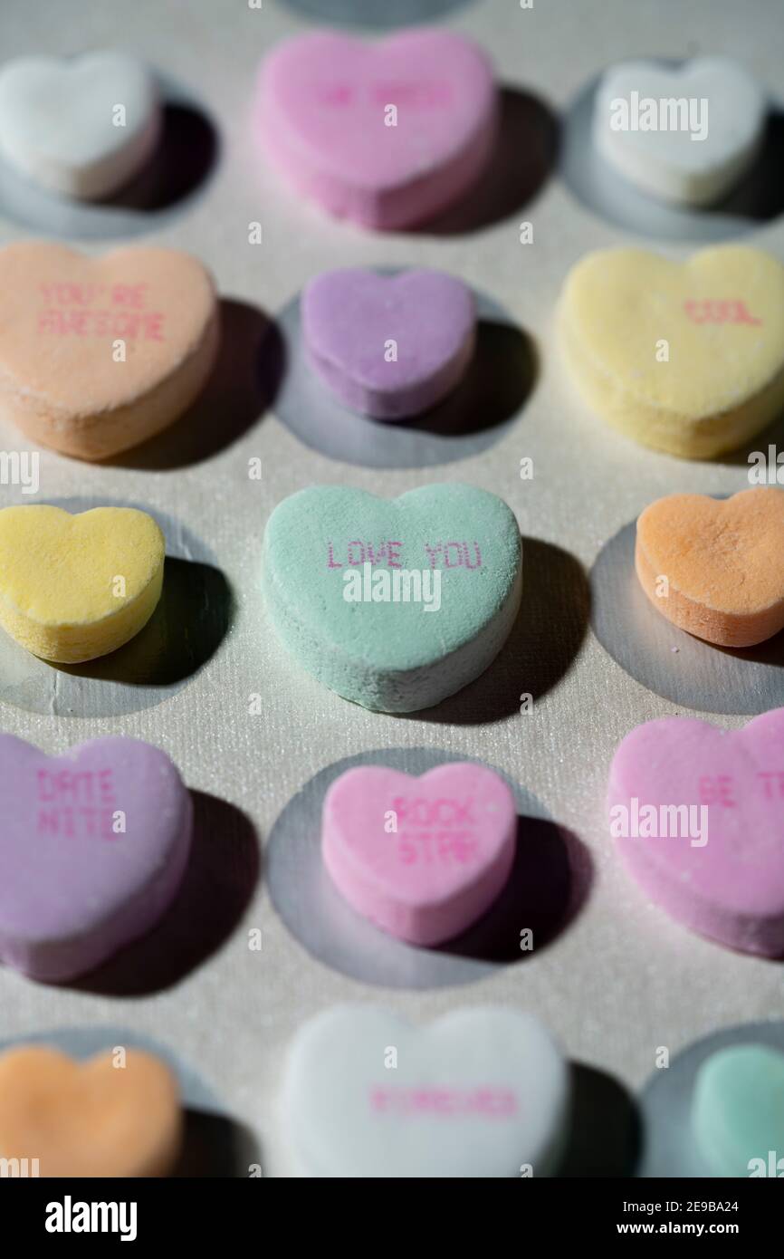 Rows of colorful conversation candy hearts lined up in rows on a white surface with one heart in focus reading 'Love You' Stock Photo
