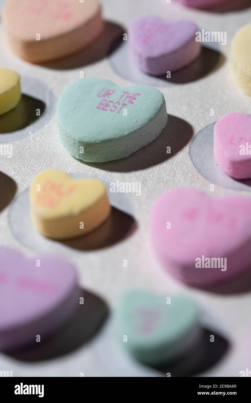 Rows of colorful conversation candy hearts lined up in rows on a white surface with one heart in focus reading 'UR The Best' Stock Photo