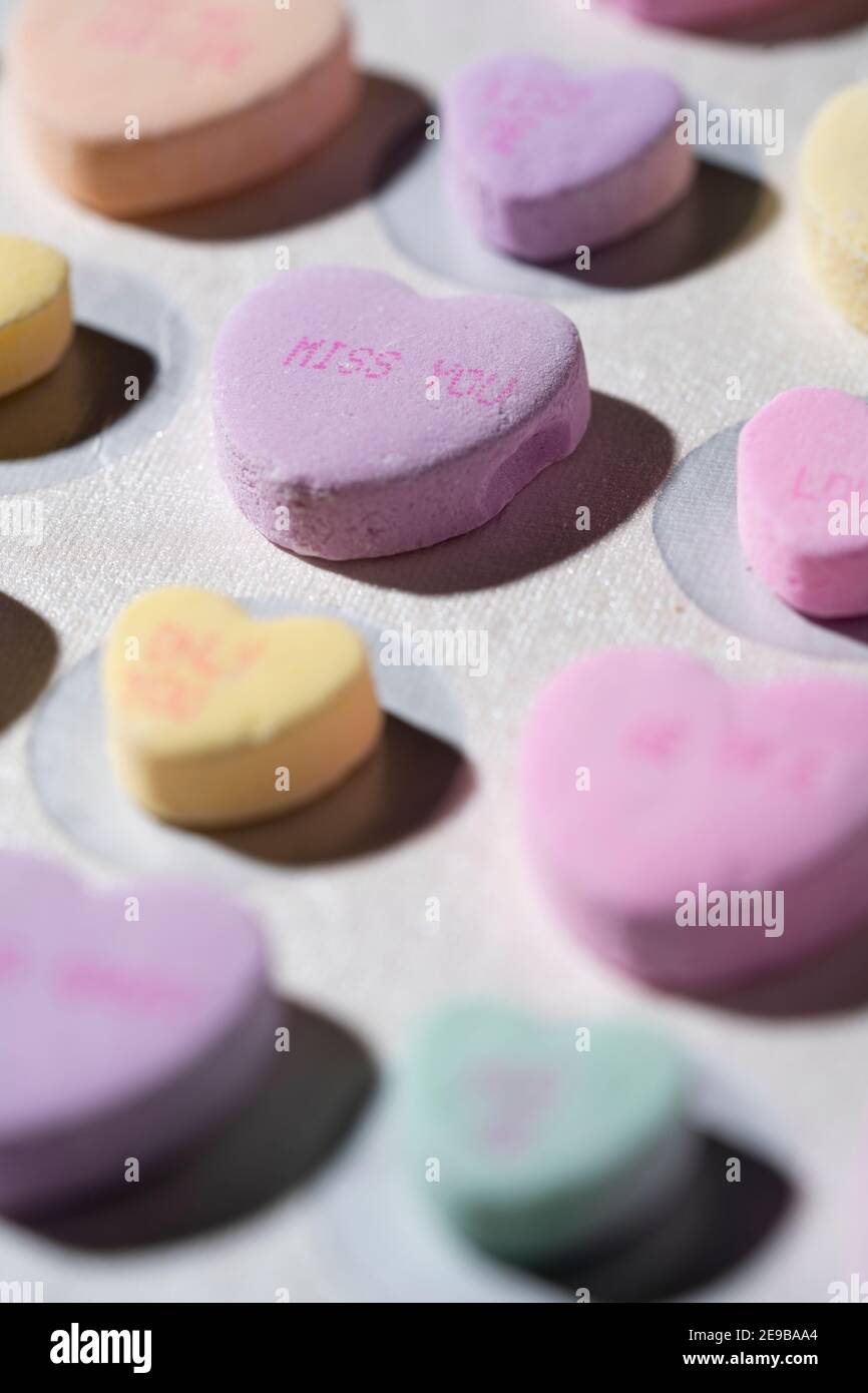 Rows of colorful conversation candy hearts lined up in rows on a white surface with one heart in focus reading 'Miss You' Stock Photo