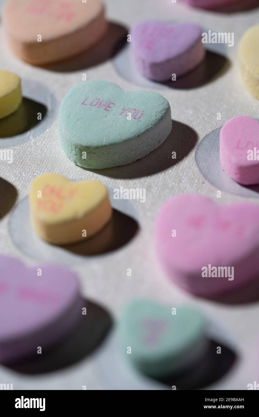 Rows of colorful conversation candy hearts lined up in rows on a white surface with one heart in focus reading 'Love You' Stock Photo