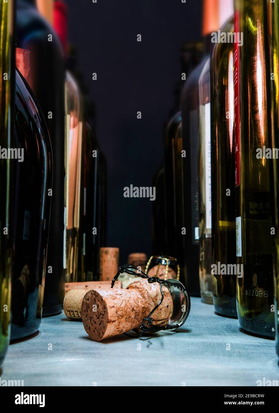 A perspective view of two rows of open wine bottles, corkscrews and corks. Low key. Stock Photo