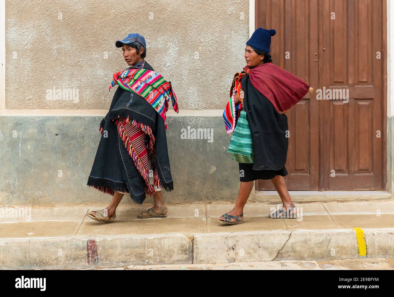 Two Bolivian Tarabuco indigenous in traditional clothing walking in a street with colonial architecture near Sucre city, Tarabuco, Bolivia. Stock Photo