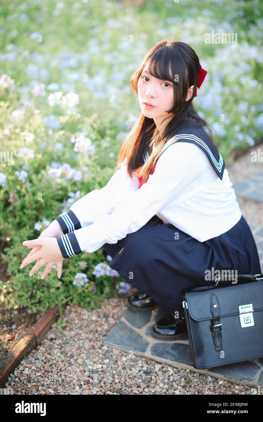 Asian school girl sitting with flower garden background Stock Photo