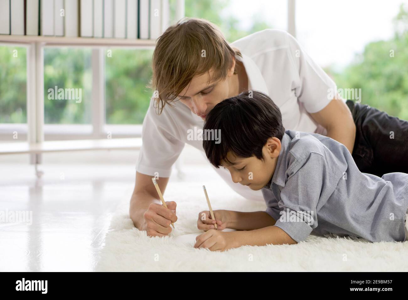 Young father taught his adopted son how to do homework in the living room during the holidays. Work life balance. Stock Photo