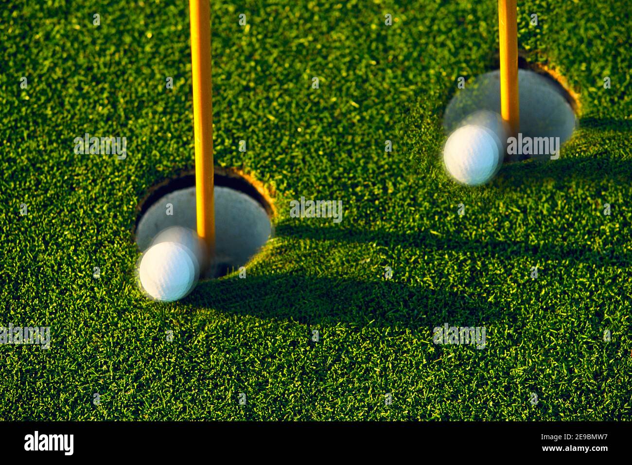 Golf balls by two holes on putting green making it confusing for the