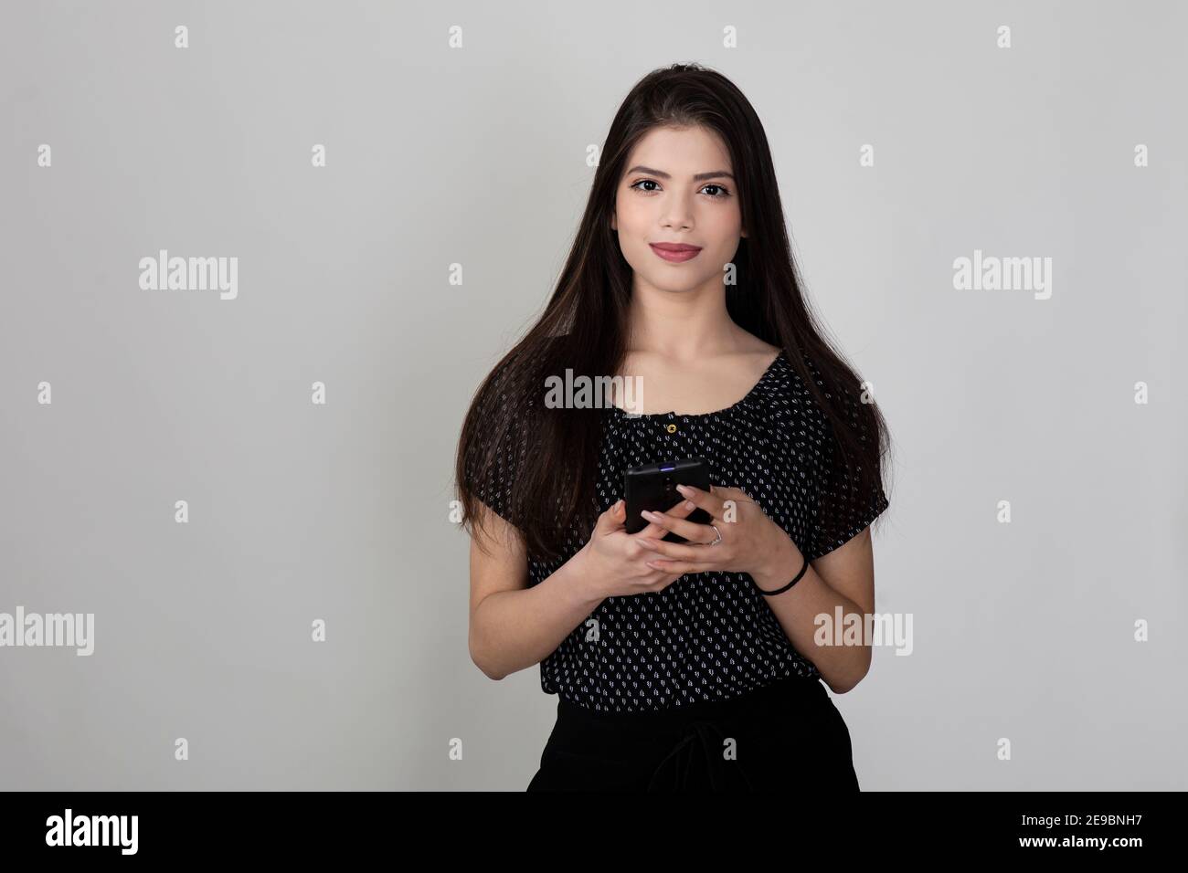 Portrait of pretty young Indian girl standing against white background and holding phone, smiling and looking into camera Stock Photo - Alamy Portrait of pretty young Indian girl standing against white background and holding phone, smiling and looking into camera Stock Photo - Alamy